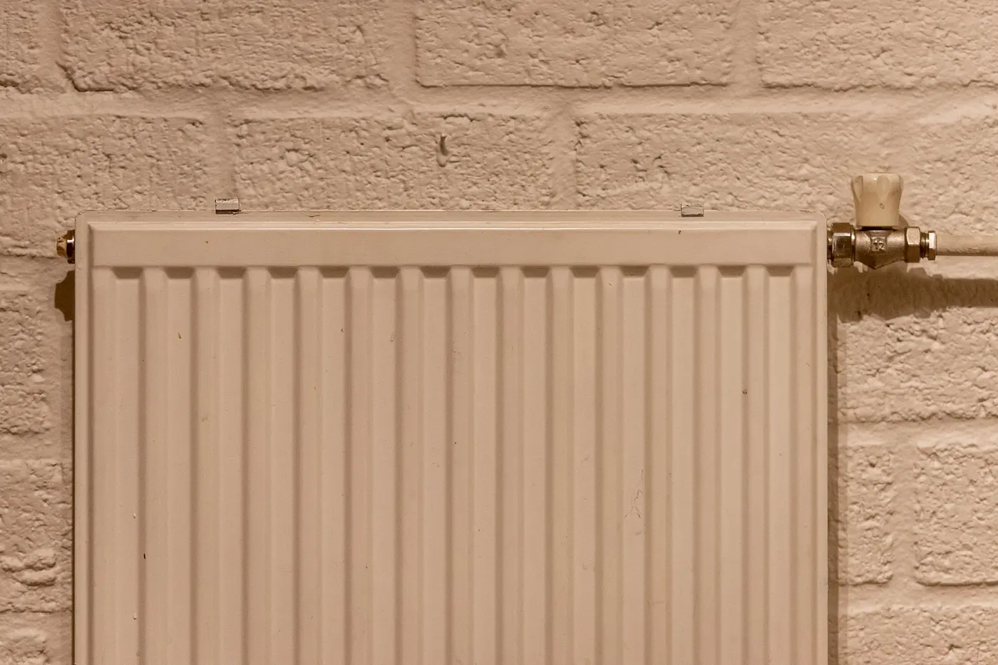 White panel radiator on a painted brick wall with a manual valve at the top right-hand end