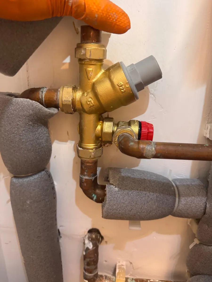 A brass combination valve and relief valve group on a cylinder being replaced by an engineer in orange gloves