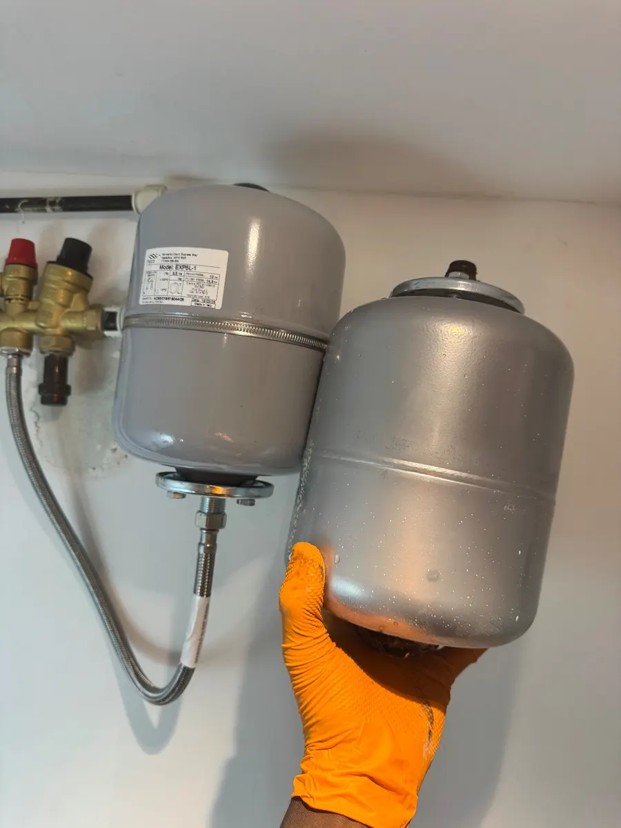 Two grey expansion vessels held side by side during a swap on an unvented cylinder