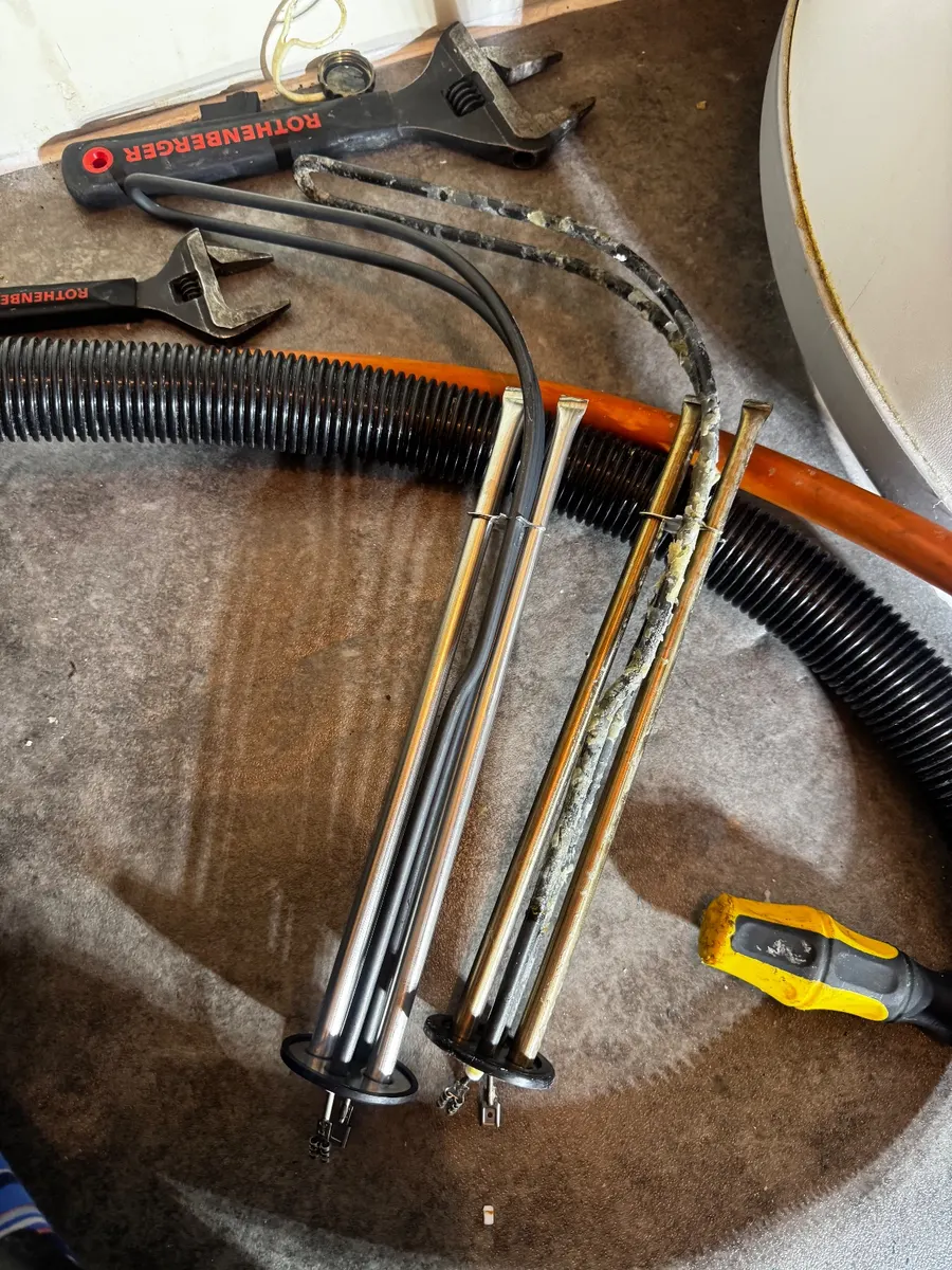 Old immersion elements removed from a hot water cylinder lying on the floor beside tools