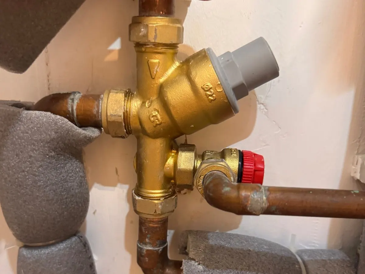 Brass pressure reducing and relief valve group on the cold feed to an unvented cylinder, with a red-capped relief valve and copper pipework