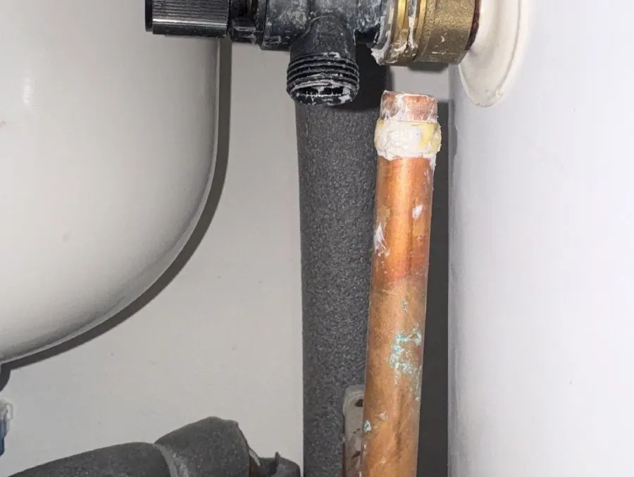 Brass safety valve fitted to the side of an unvented cylinder with a short copper pipe below it, beside an expansion vessel