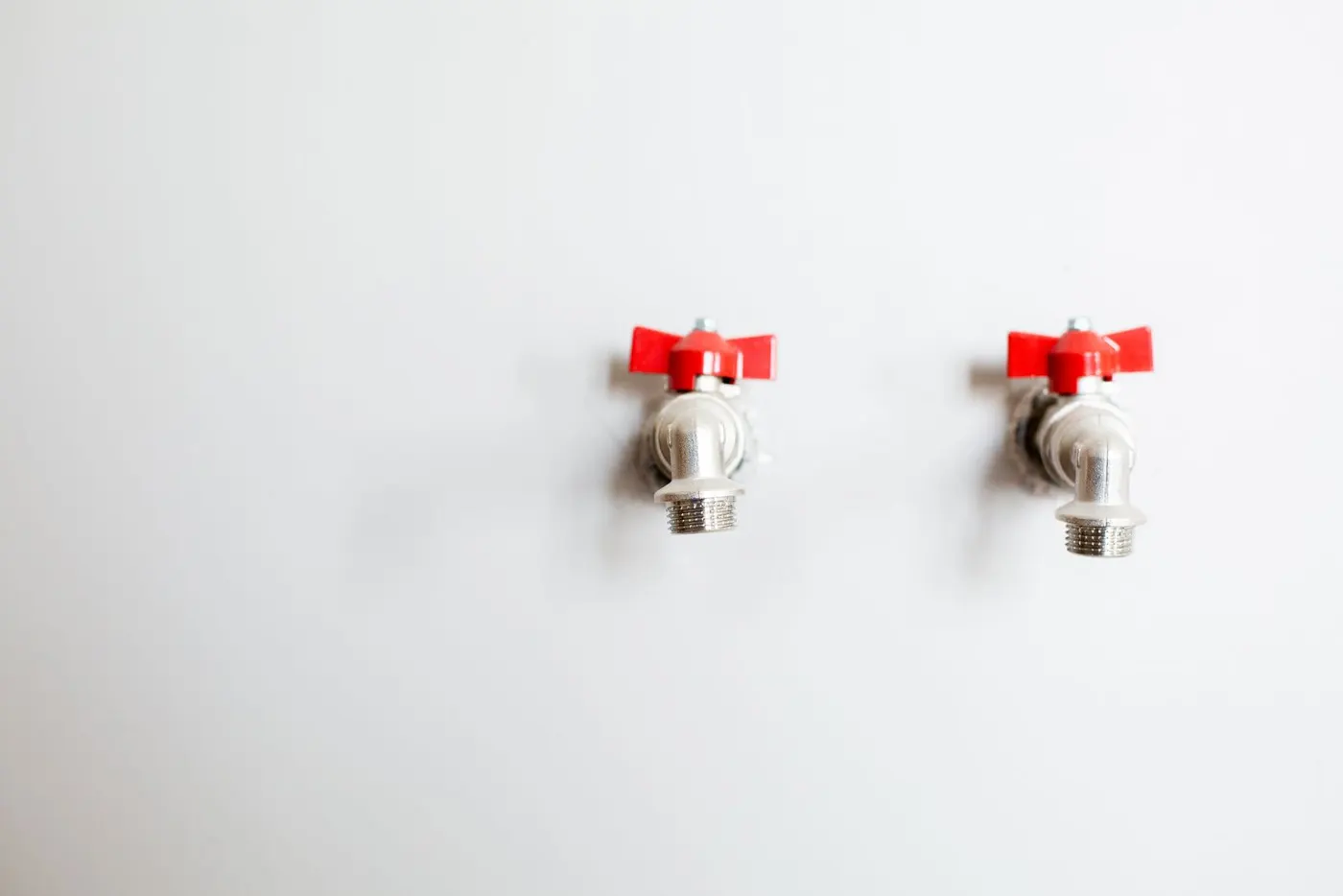 Two quarter-turn water supply valves with red butterfly handles coming out of a white wall